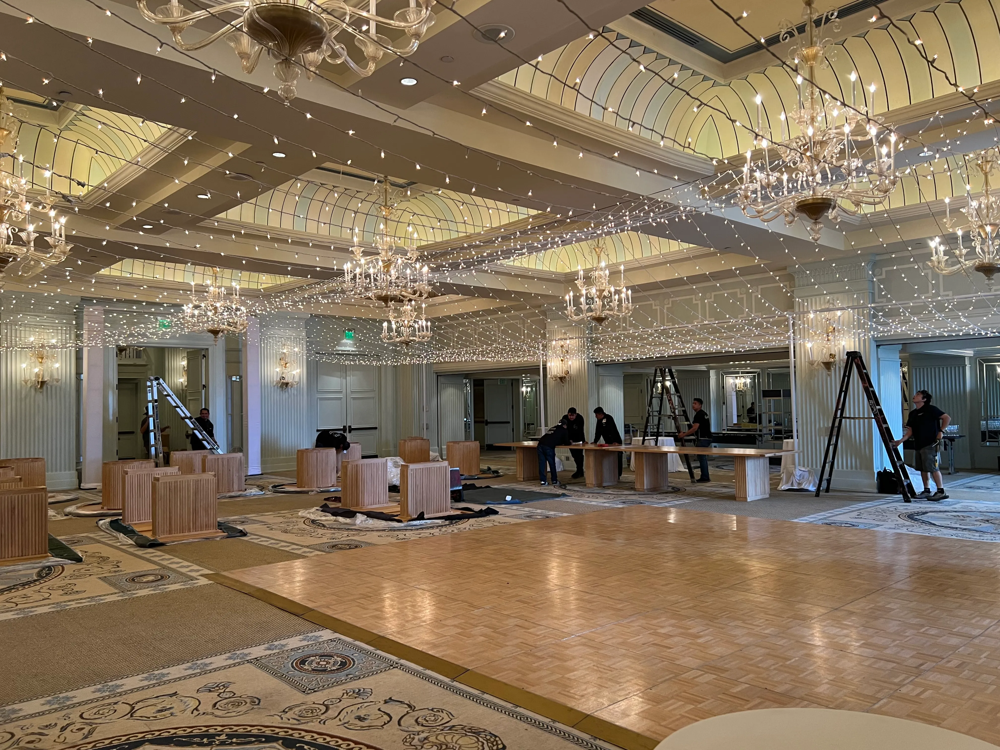Lighting crew on ladders installing a twinkle light canopy in an ornate hotel ballroom