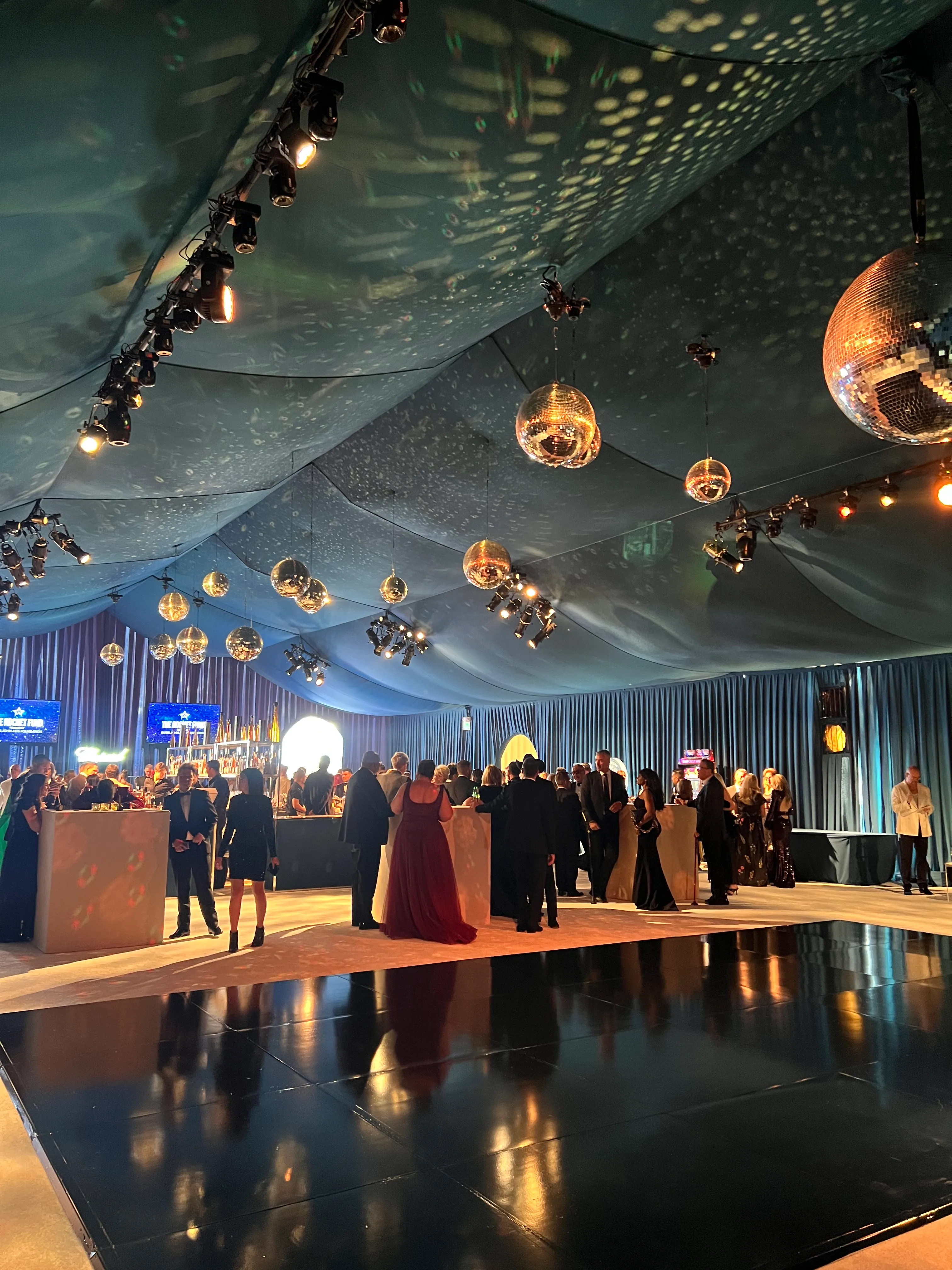 Black-tie fundraiser in a deep blue draped tent with mirror balls and warm textured ceiling light