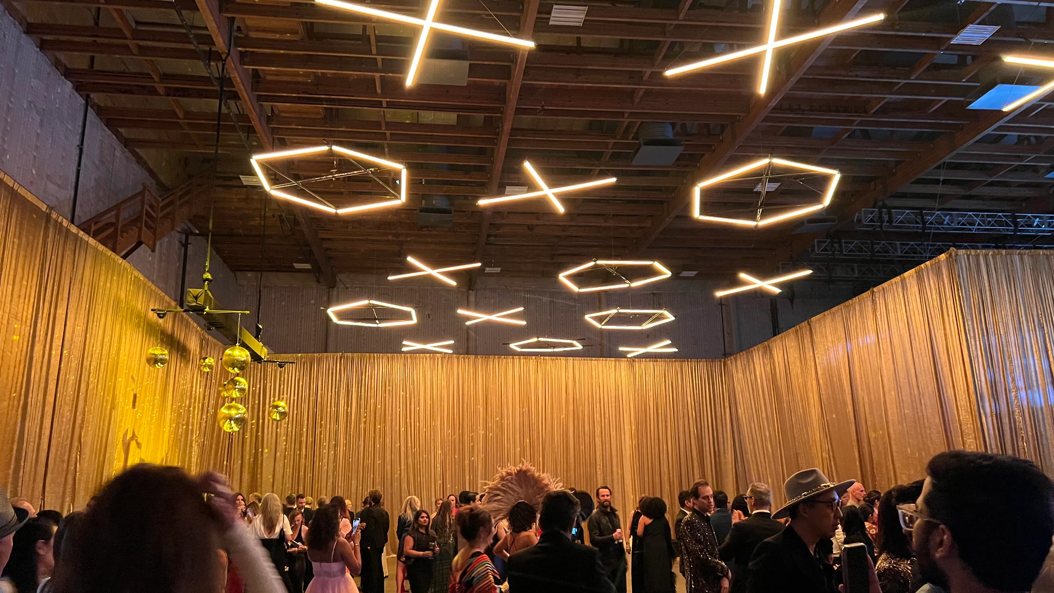 Custom geometric tube-light installation suspended over a gold-draped event space