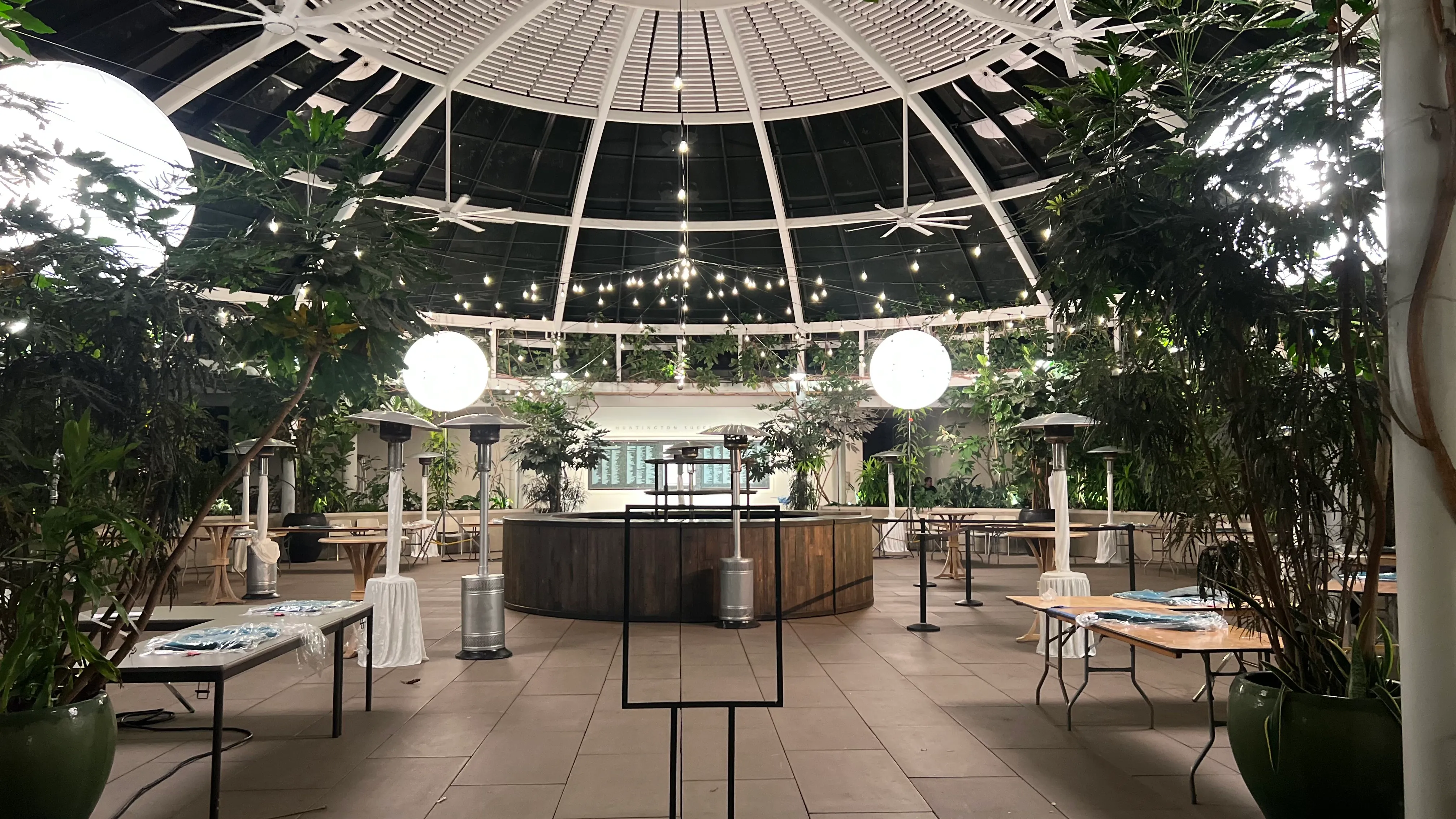 Glass conservatory dome with string lights and glowing globe lanterns among greenery
