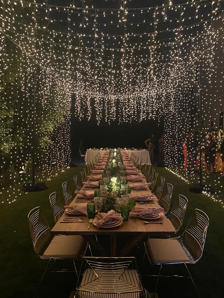 Long garden dinner table surrounded by curtains of twinkle lights