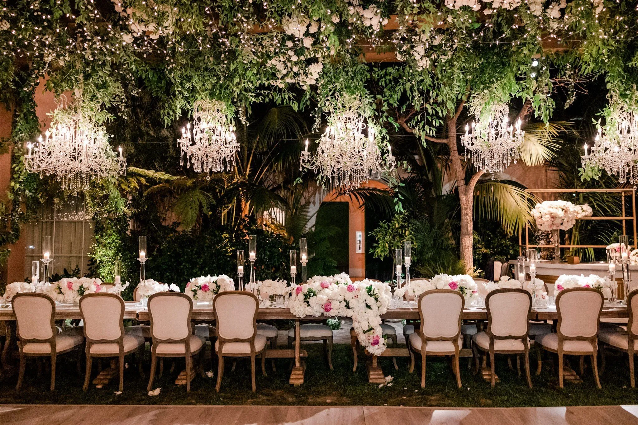 Garden wedding dinner beneath crystal chandeliers and twinkle lights woven through greenery