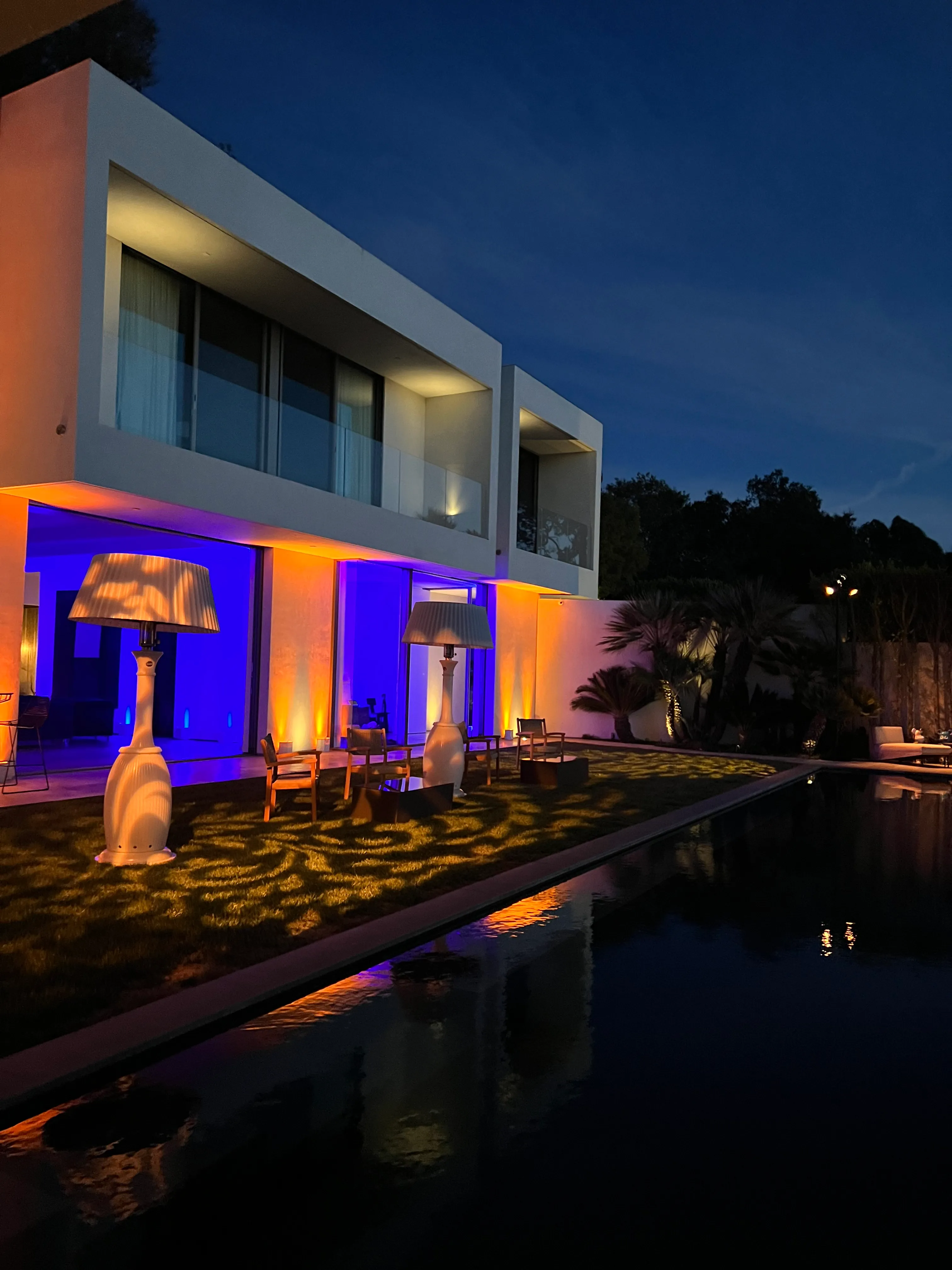 Modern estate at dusk with amber and blue uplighting reflected in the pool