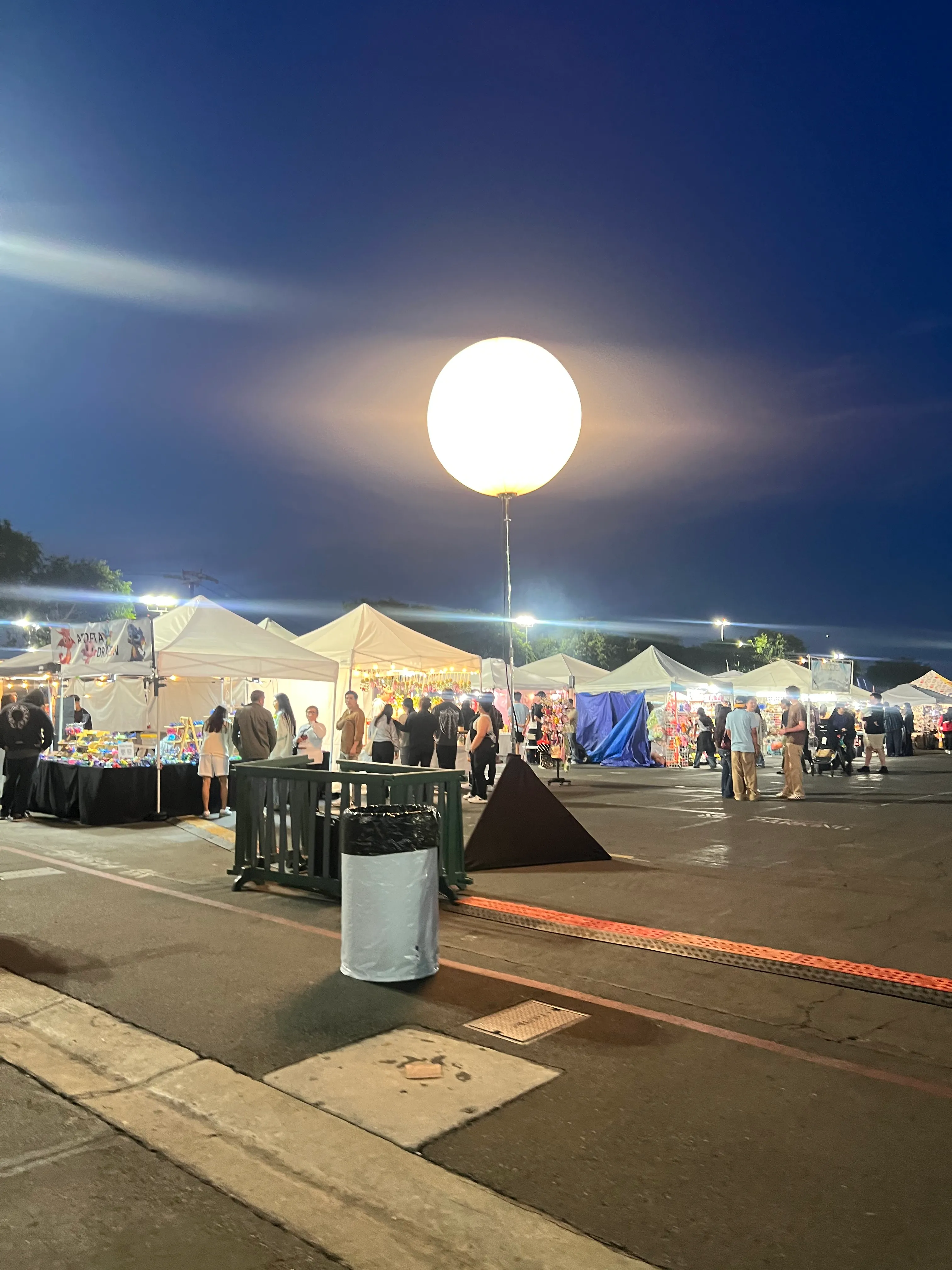 Glowing balloon light tower over vendor tents at an evening market
