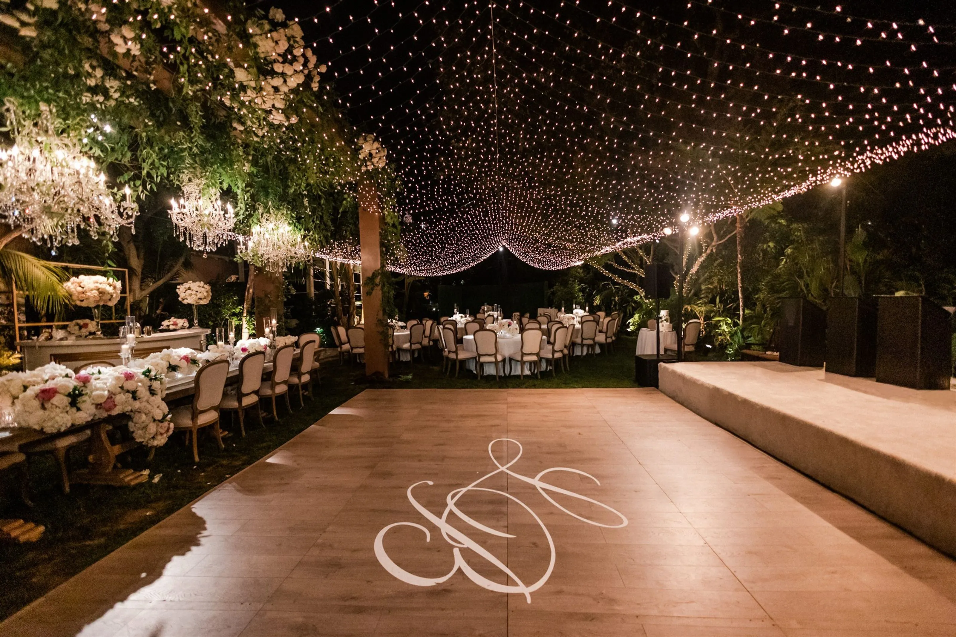 Outdoor evening dinner reception lit with string lights and a custom monogram light projection