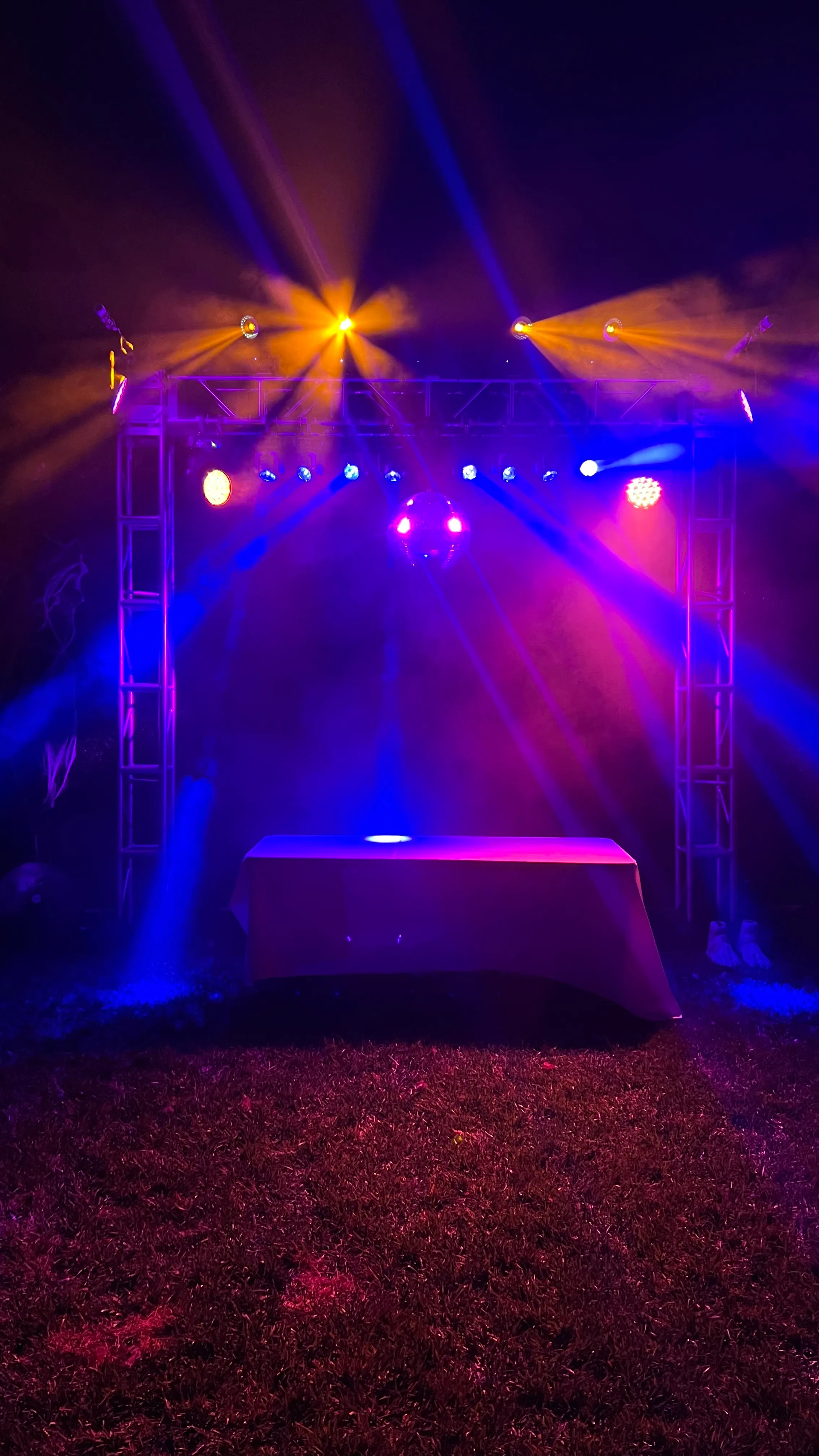 Backyard party stage with truss, colored beams, haze, and a mirror ball at night