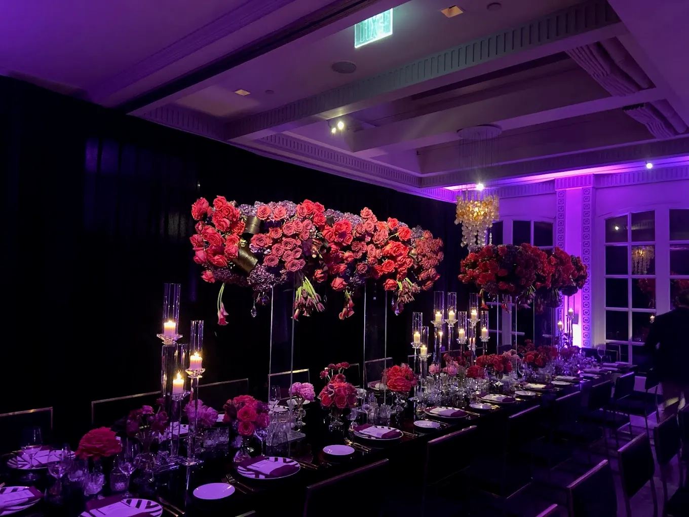 Long dinner table with tall red rose centerpieces, candles, and violet uplighting