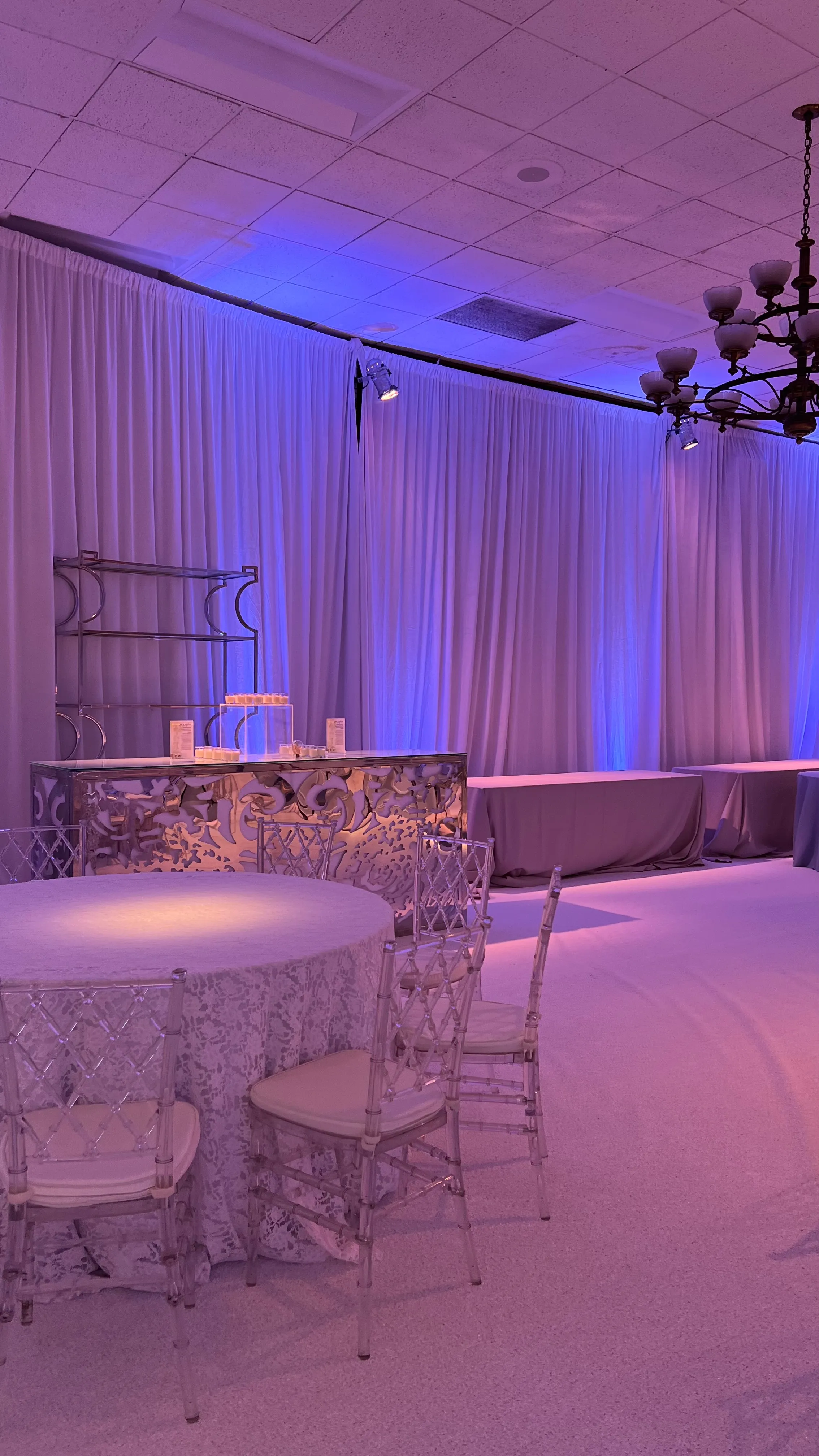 Draped reception room washed in soft pink and violet uplighting