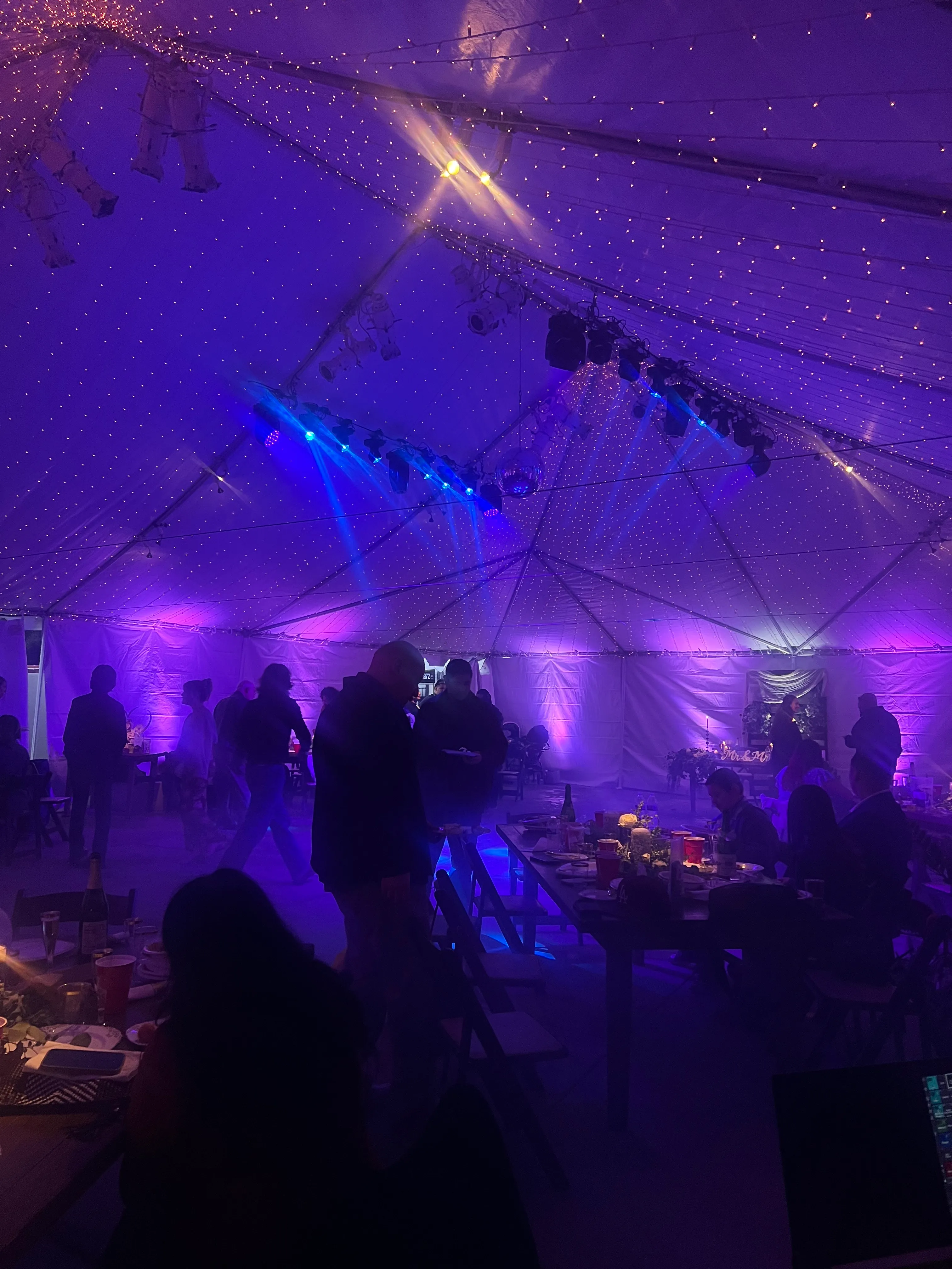 Tented party with blue beam effects and twinkle lights over a crowded dance floor